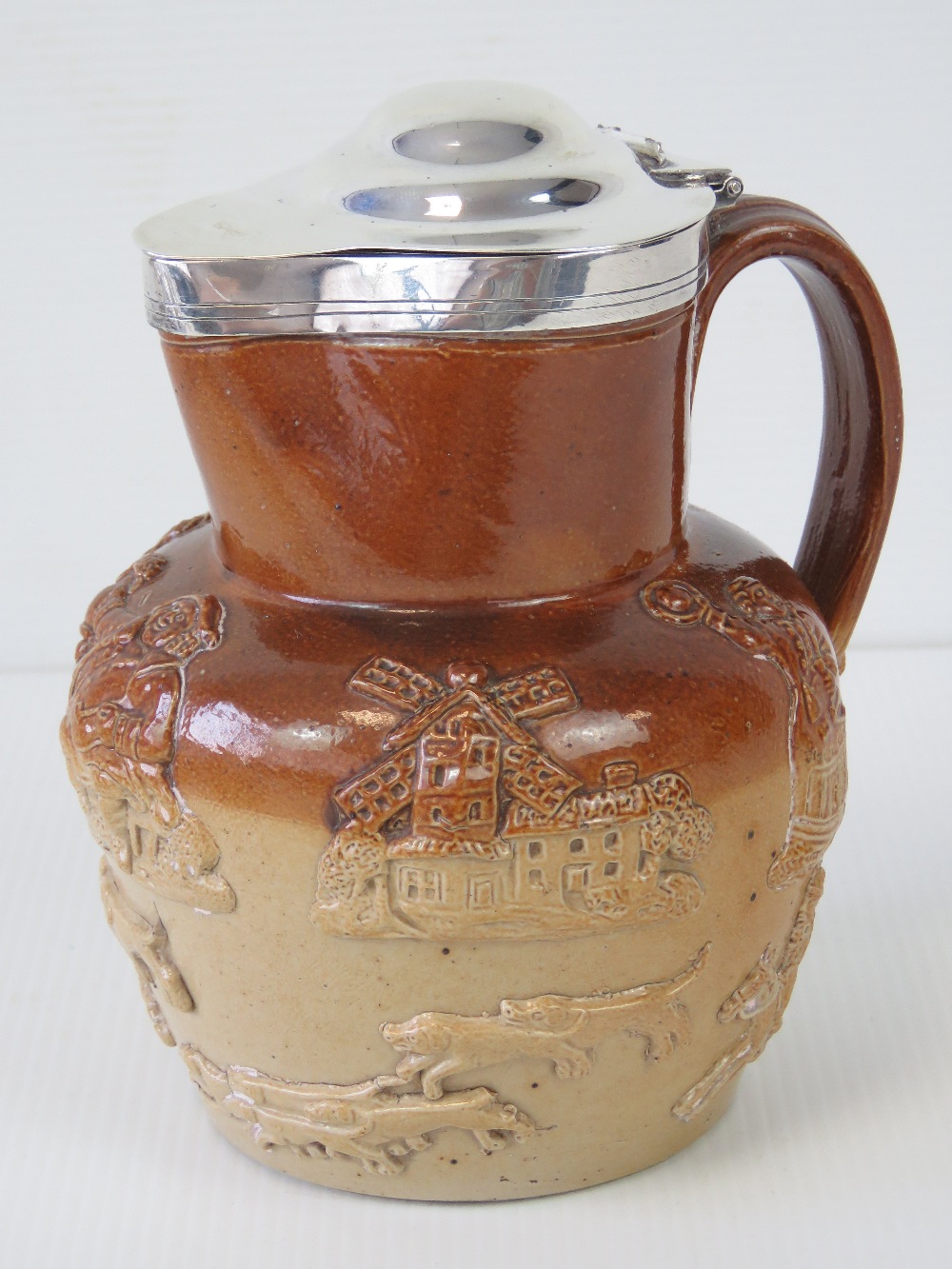 A Victorian salt glazed stoneware jug with HM silver lid, having hunting dogs, windmill, etc upon,