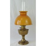 A brass oil lamp having clear glass chimney and orange glass dome shade, standing 60cm high.