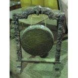 A large gong suspended from a H shaped carved frame having fruit and foliate decoration and central