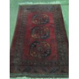 A red ground Middle Eastern rug having three central medallions, approx 107 x 180cm.