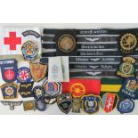 Thirty-five military and police cloth badges, arm band and cuff titles, various ages and countries.