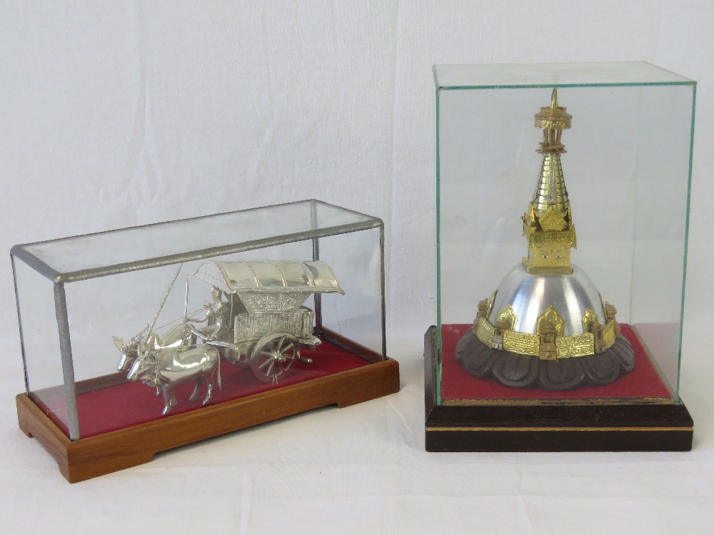 A white metal bullock cart with driver, stamped 800, upon wooden stand with glass cover,