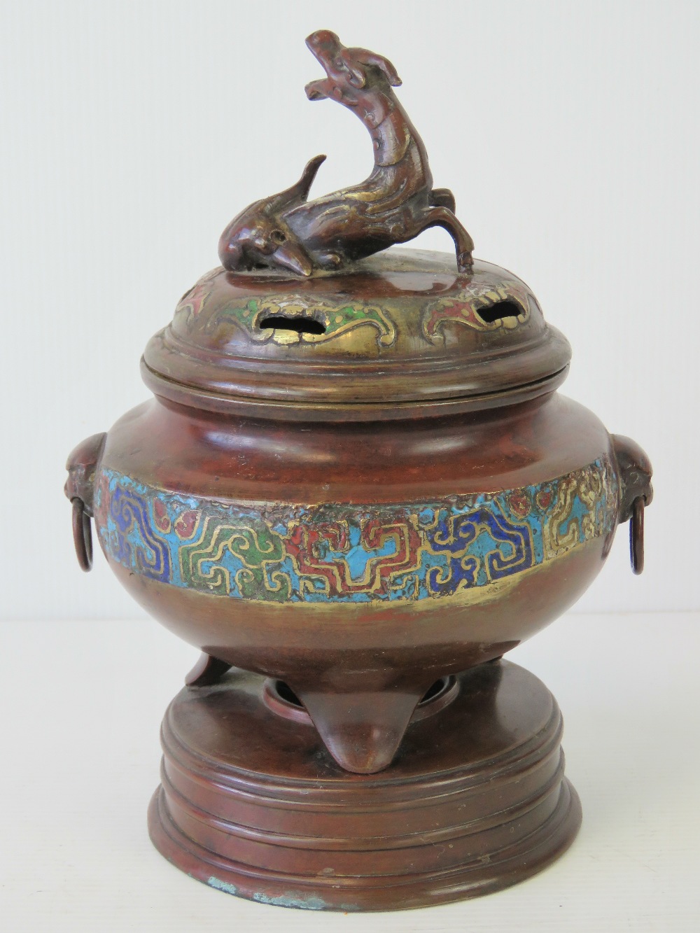 A fine bronze Oriental lidded censer having a band of cloisonné decoration and raised over three