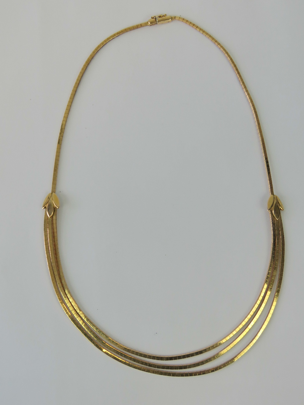 An 18ct gold articulated necklace having central trio of graduated snake link chain with triform - Image 2 of 3