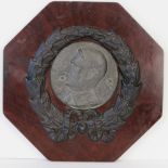 A white metal plague bearing the portrait of Hitler, mounted on board with wreath, 30cm wide.
