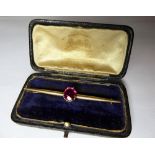 An 18ct Gold bar brooch with a centrally mounted claw set bright pink semi precious stone.