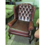 A good winged button back red leather armchair, having loose cushion.