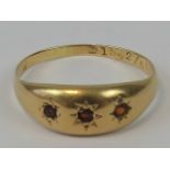 A yellow metal and garnet gypsy ring having three graduated garnets in star settings,