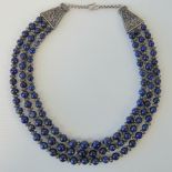 A lapis lazuli necklace comprising three graduated strands of lapis lazuli beads with white metal