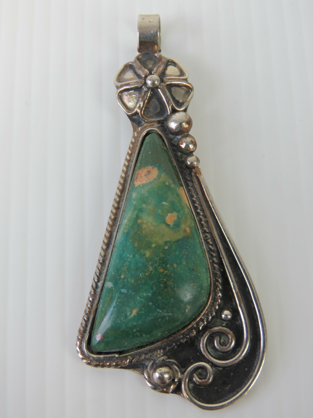 A hand made pendant having triangular green agate in floral white metal setting, 7cm in length.