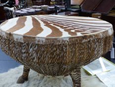 AN AFRICAN ZEBRA HIDE COVERED DRUM ON THREE HOOF LEGS.