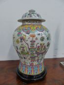 A FAMILLE ROSE DECORATED COVERED BALUSTER FORM VASE WITH A CARVED STAND. OVERALL H.50cms.