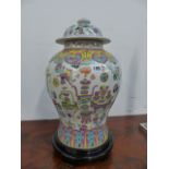 A FAMILLE ROSE DECORATED COVERED BALUSTER FORM VASE WITH A CARVED STAND. OVERALL H.50cms.