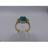 A 585 STAMPED PRECIOUS YELLOW METAL EMERALD AND DIAMOND THREE STONE RING. THE CENTRAL STONE BEING AN