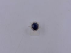 A 585 STAMPED WHITE METAL SAPPHIRE AND DIAMOND CLUSTER RING. THE OVAL SAPPHIRE IS IN A FOUR CLAW