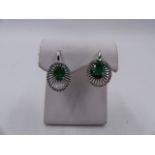 A PAIR OF EMERALD AND DIAMOND LEVER BACK WHITE METAL EARRINGS. THE OVAL EMERALD IS HELD IN A FOUR