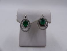 A PAIR OF EMERALD AND DIAMOND LEVER BACK WHITE METAL EARRINGS. THE OVAL EMERALD IS HELD IN A FOUR