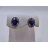 A PAIR OF WHITE METAL SAPPHIRE AND DIAMOND STUD EARRINGS. EACH OVAL SAPPHIRE IS SUSPENDED IN A
