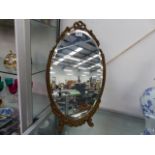 AN OVAL DECORATIVE GUILDED MIRROR ON STAND.