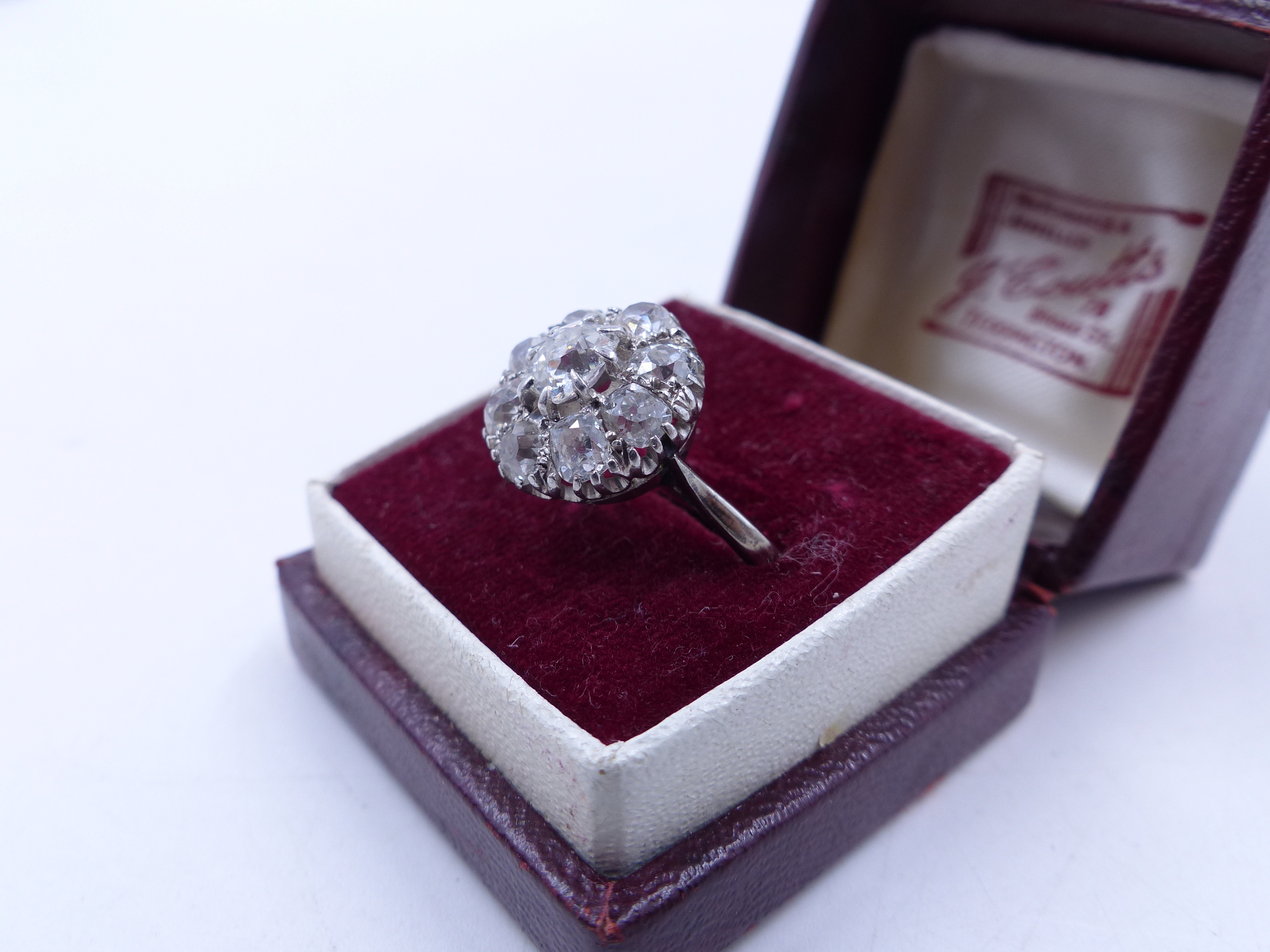 AN OLD CUT DIAMOND CLUSTER RING IN A WHITE METAL SETTING (TESTED AS WHITE GOLD). THE CENTRAL DIAMOND
