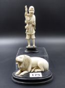 AN ORIENTAL CARVED FIGURE OF A RECUMBENT LION ON OVAL HARDWOOD BASE L.09cms TOGETHER WITH A STANDING