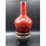 A CHINESE SANG DE BOUEF BOTTLE FORM VASE TOGETHER WITH A CARVED HARDWOOD STAND. H.31cms