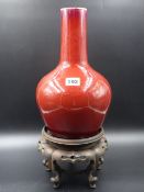 A CHINESE SANG DE BOUEF BOTTLE FORM VASE TOGETHER WITH A CARVED HARDWOOD STAND. H.31cms