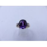 A 9CT YELLOW GOLD PURPLE SAPPHIRE RING. THE CENTRAL PURPLE SAPPHIRE IS AN OVAL CUT IN A FOUR CLAW