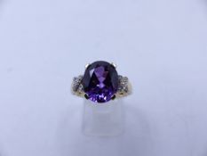 A 9CT YELLOW GOLD PURPLE SAPPHIRE RING. THE CENTRAL PURPLE SAPPHIRE IS AN OVAL CUT IN A FOUR CLAW