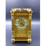 A VICTORIAN CASED CARRIAGE CLOCK WITH FLORAL CHASED DECORATIVE DIAL AND ENAMEL CHAPTER RING.