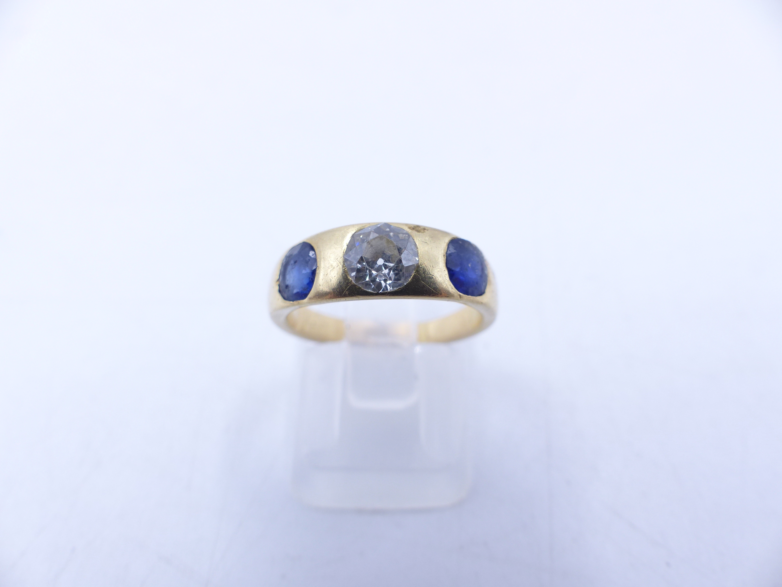 AN 18 STAMPED YELLOW GOLD SAPPHIRE AND DIAMOND THREE STONE TRADITIONAL GYPSY-SET RING. THE CENTRE