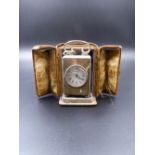 A SILVER CASED CARRIAGE OR DRESSING TABLE CLOCK WITH ORIGINAL PROTECTIVE LEATHER CASE.