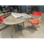 A CIRCULAR TEAK PATIO TABLE, PARASOL AND A FOLDING CHAIR.