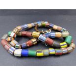 A GRADUATED ROW OF ANTIQUE GLASS AND HARDSTONE TRIBAL CYLINDRICAL TRADE BEADS, LENGTH 80cms.