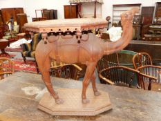 A FINELY CARVED TEAK CAMEL FORM OCCASIONAL TABLE WITH OCTAGONAL TOP. 85cms OVERALL AND H.75cms