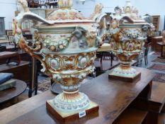 A PAIR OF DECORATIVE CONTINENTAL POTTERY LARGE FIGURAL TWIN HANDLE COVERED URNS, POLYCHROME