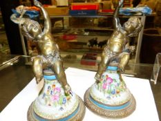 A PAIR OF CANDLESTICKS, THE BRONZE CHERUBS HOLDING UP NOZZLES WHILE SEATED ON CONES OF PORCELAIN