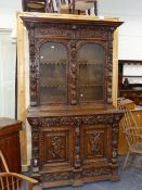 A CARVED OAK FLEMISH BOOKCASE CABINET WITH TWO DOOR GLAZED UPPER SECTION ABOVE A PANELLED DOOR