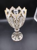 A BOHEMIAN WHITE OVERLAY GLASS VASE, THE GOBLET SHAPE WITH SERRATED GILT LINED RIM ABOVE BUN KNOP