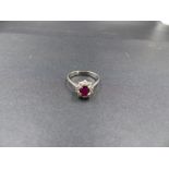 A RUBY AND DIAMOND CLUSTER RING, STAMPED 750, TESTED AS 18ct WHITE GOLD. THE CENTRAL OVAL RUBY IS