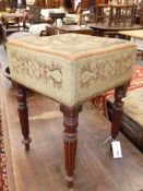 AN EARLY VICTORIAN MAHOGANY STOOL WITH NEEDLEWORK UPHOLSTERY ON REEDED TURNED LEGS.