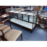 A GOOD VINTAGE MAHOGANY AND BRASS FRAMED GLASS SHOP COUNTER WITH FITTED SHELVES AND FOUR DOORS.