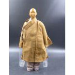 A CHINESE DOOR OF HOPE MISSION CARVED WOODEN DOLL CLOTHED IN A BROWN COAT OVER A BLUE SUIT.