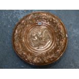 A COPPER REPOUSSE DISH DECORATED WITH FOLIAGE ENCLOSING THE CENTRAL GRIFFIN. DIA.51CMS.