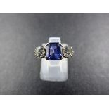 AN 18CT STAMPED CEYLON BLUE SAPPHIRE AND DIAMOND THREE STONE RING. THE CENTRAL SAPPHIRE IS A