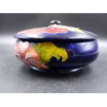 A MOORCROFT COVERED BOWL DECORATED WITH HIBISCUS FLOWERS AND FOLIAGE ON A MIDNIGHT BLUE