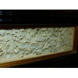 A CHINESE IVORY PLAQUE CARVED IN RELIEF WITH A VILLAGE SCENE WITHIN AN EBONISED FRAME. 6.5 X 18.