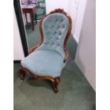 A CARVED WALNUT BUTTON BACK VICTORIAN LADIES CHAIR WITH FLORAL CREST AND APRON ON CABRIOLE LEGS.