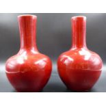 TWO CHINESE SANG DE BOEUF BOTTLE VASES, ONE WITH THE WIDER DIAMETER NECK WITH A MOTTLED RED GLAZE.