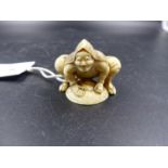 A JAPANESE IVORY NETSUKE CARVED AS A MAN SQUATTING LEANING WITH HIS HANDS ON HIS STRAW HAT,